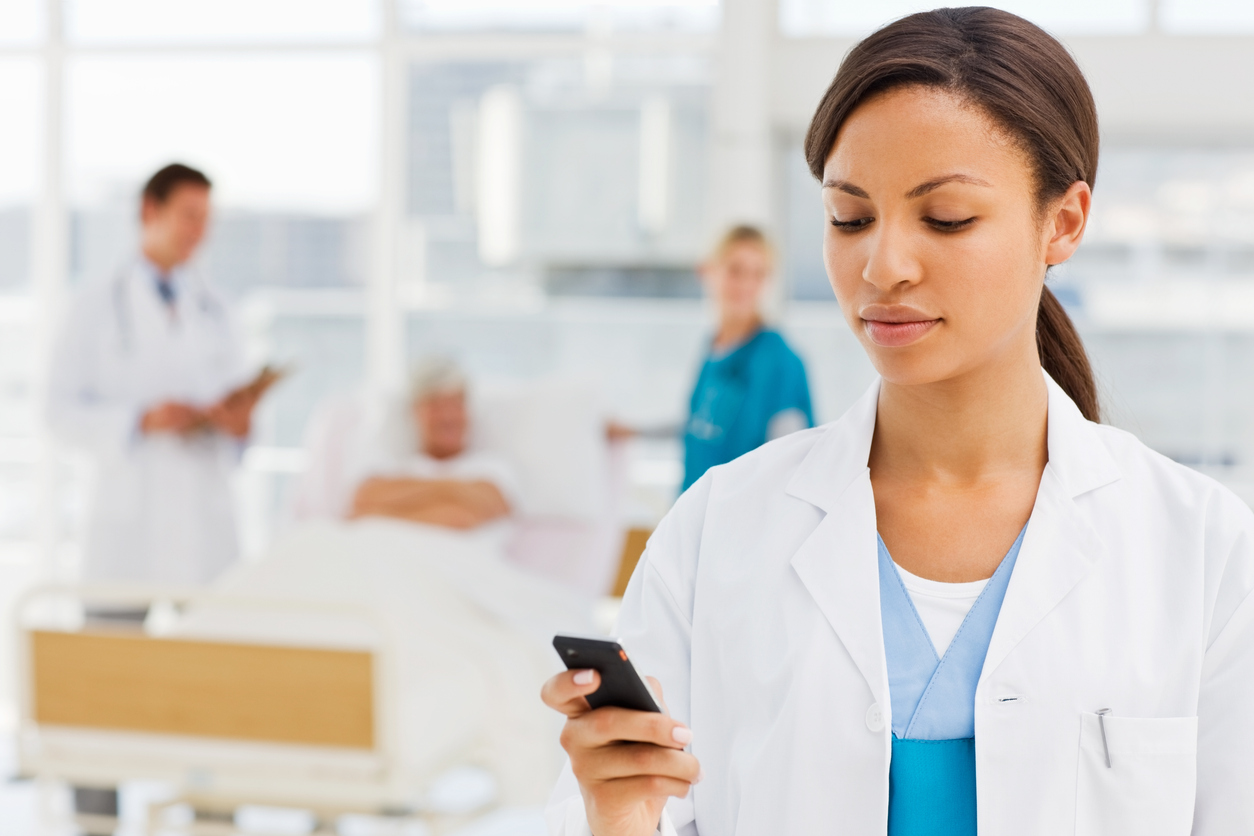 Female doctor holding cellphone with colleagues and patient in background